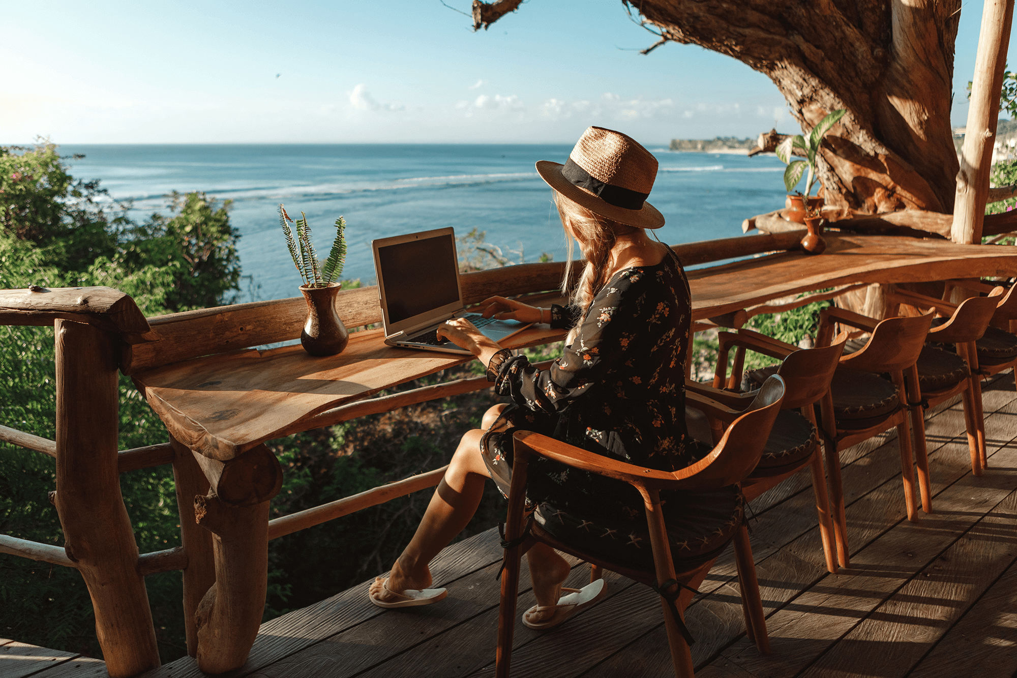 Woman working on laptop on oceanfront deck.